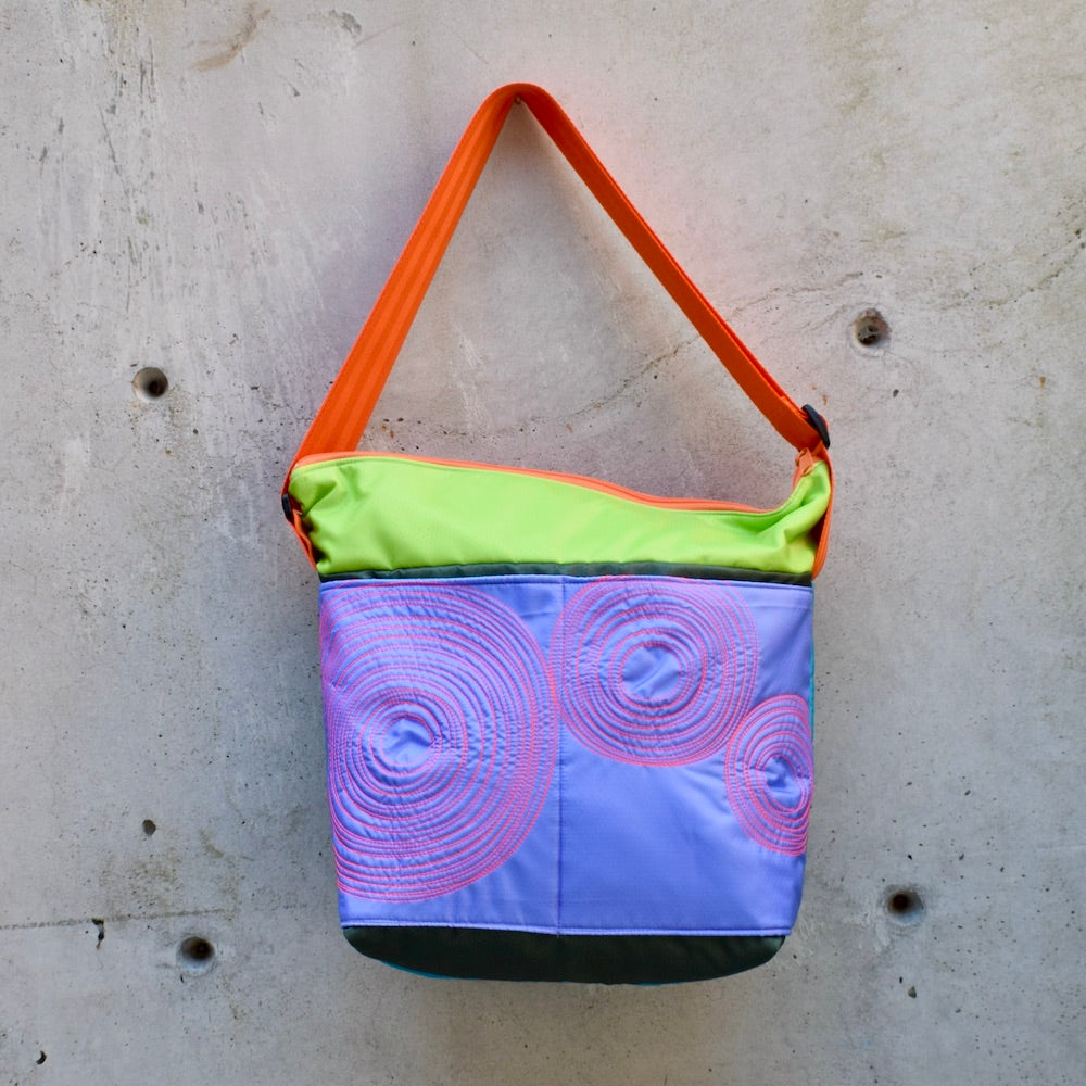 large zippered bag with outer pockets, cross body bag. adjustable strap, two interior pockets,  two exterior pockets, YKK zipper, made in canada, made in toronto, handmade, one of a kind, topstitching, spirals, perfect for travel, perfect everyday, work, gym, play, travel, durable, lightweight, machine washable, multicoloured, army green, mauve, lime with a orange strap